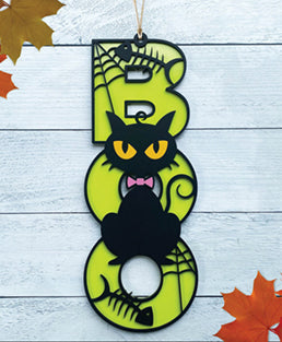 BOO wooden door sign featuring the letters B O O in a vertical format with various Halloween images pictured on top of the BOO. This one features a black cat with yellow eyes and a pink bow tie. 