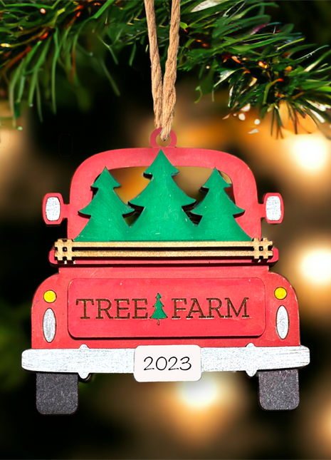 Red wooden truck ornament with "Tree Farm" engraved on tailgate. There are three Christmas trees in the back of the truck. The license plate reads 2023.