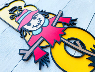 BOO wooden door sign featuring the letters B O O in a vertical format with various Halloween images pictured on top of the BOO. This one features a scarecrow. 