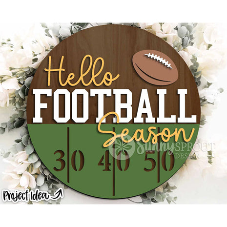 Round wooden door hanger "Hello Football Season." The bottom half features green to indicate grass and markings for the 30, 40 and 50 yard lines. There is a football at the top of the hanger.
